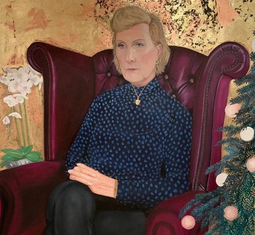 Portrait of woman in blue polka-dot blouse seated on burgundy armchair with orchids and festive tree
